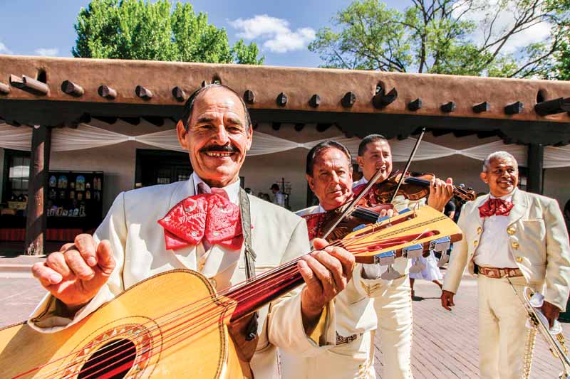 Four Mariachi band members smile at the camera as they play.