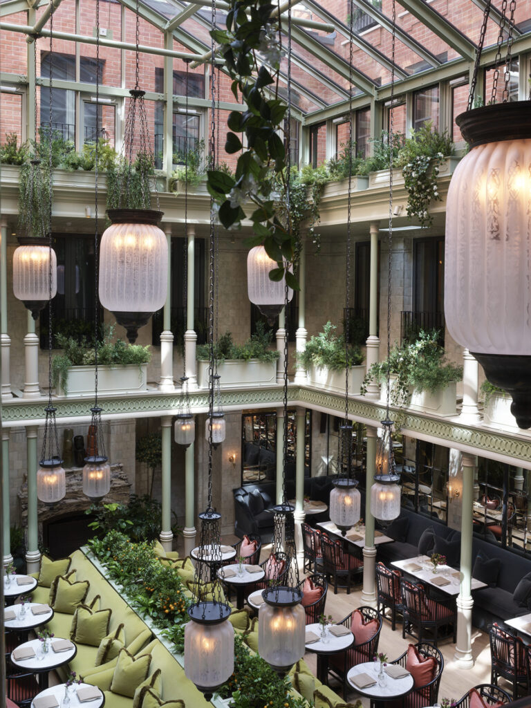 The atrium features hanging lamps strung from a high ceiling, with varied dining options below. Plants adorn the space.
