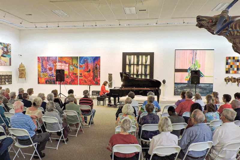 People sitting on chairs watching a pianist play inside the museum.