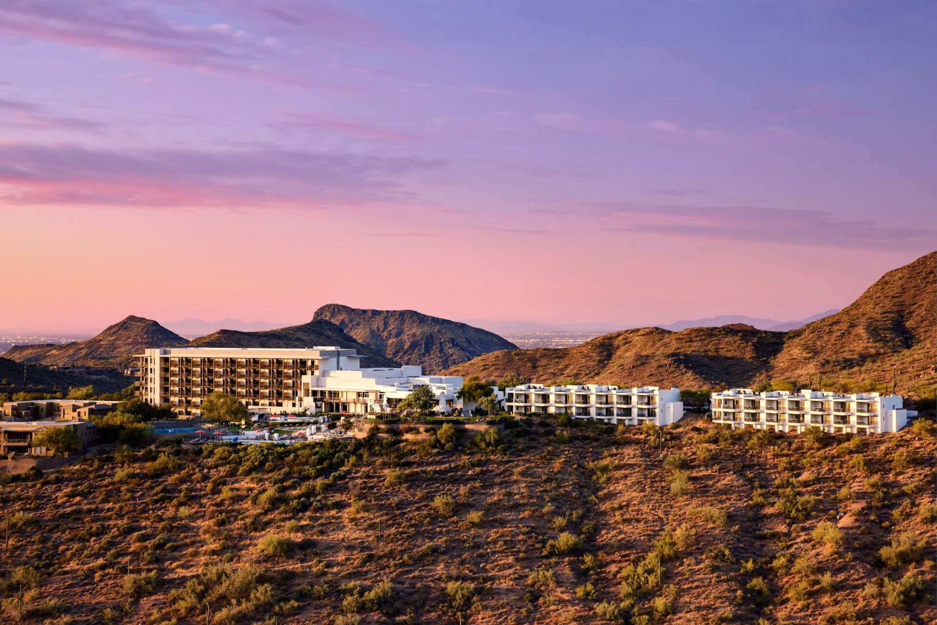 Exterior view of ADERO Scottsdale Resort nestled in the Sonoran Desert at sunset, with rugged mountains and a pink-and-purple sky in the background.
