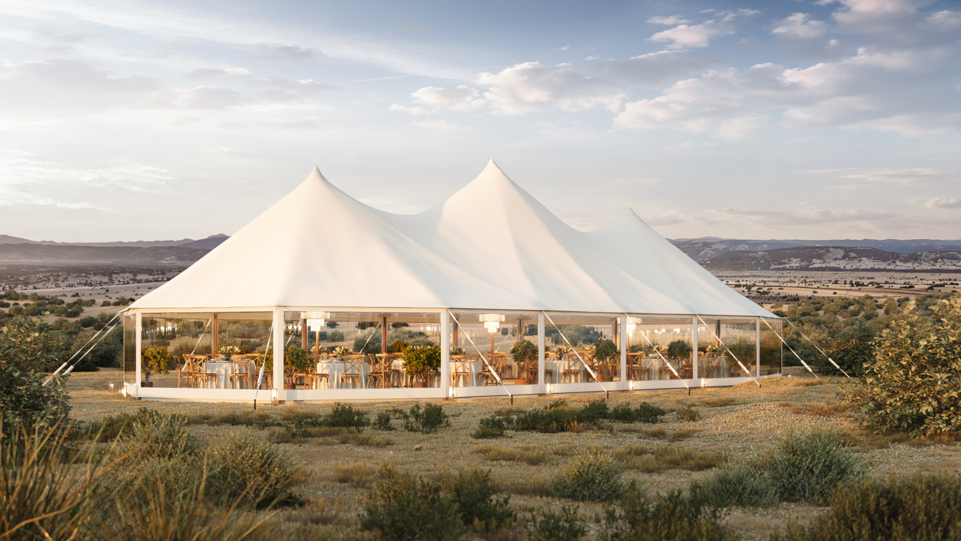 Event tent with a peaked white canopy and transparent walls, set in a high-desert landscape with mountains in the distance.