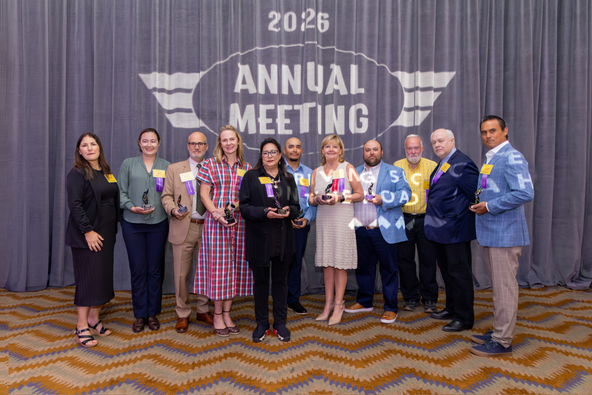 A group of 11 people pose onstage holding awards at Visit Albuquerque’s 2026 Annual Meeting, with an “Annual Meeting” backdrop behind them.